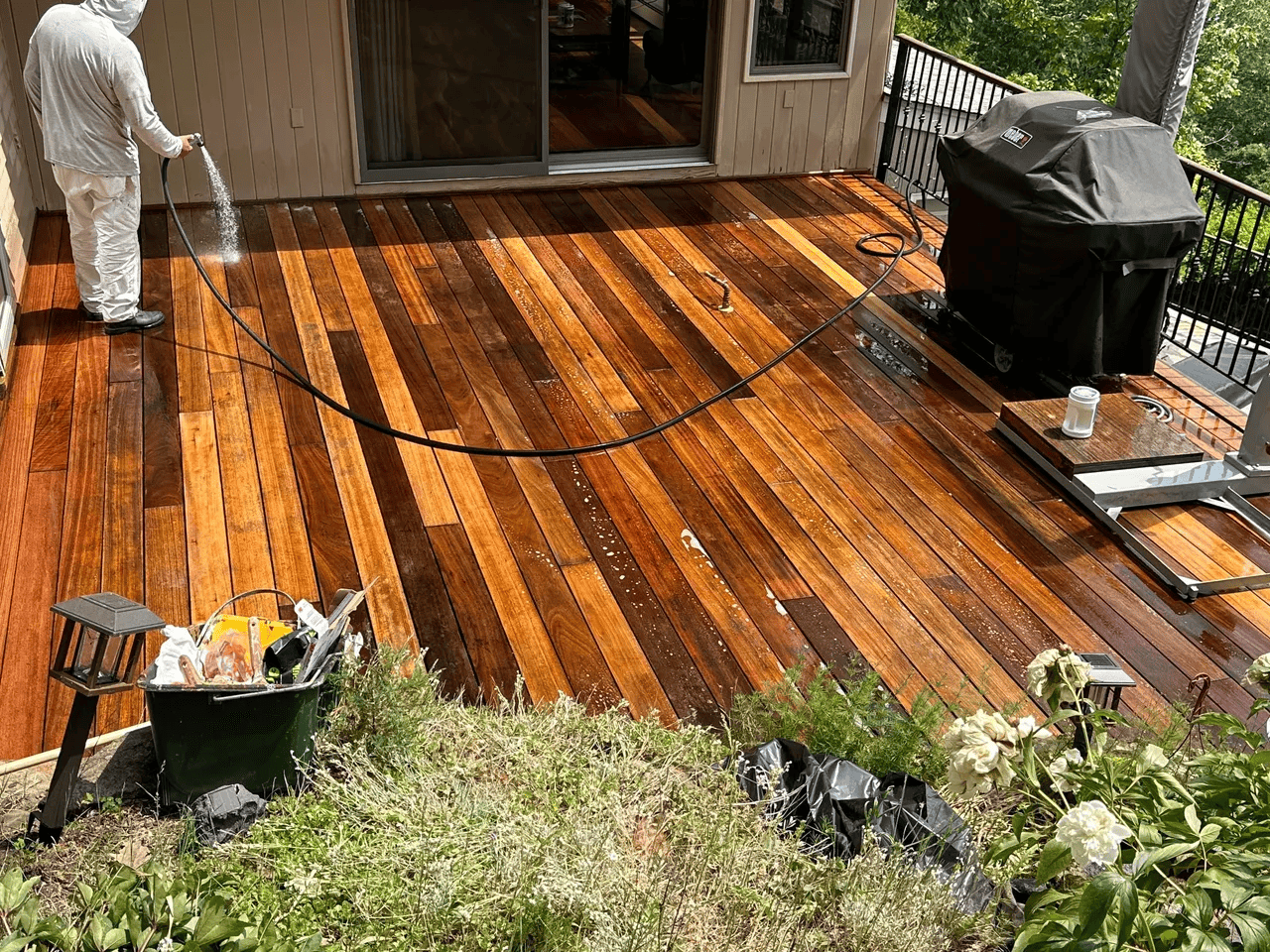 A man is cleaning a wooden deck with a hose.