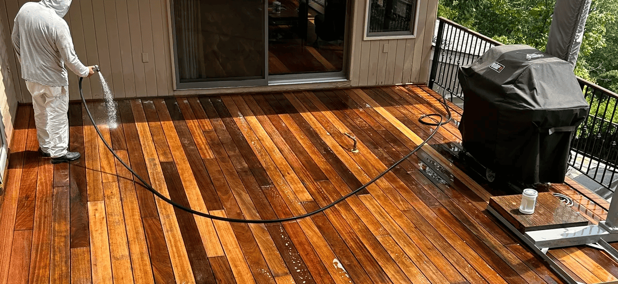 A man is cleaning a wooden deck with a hose.