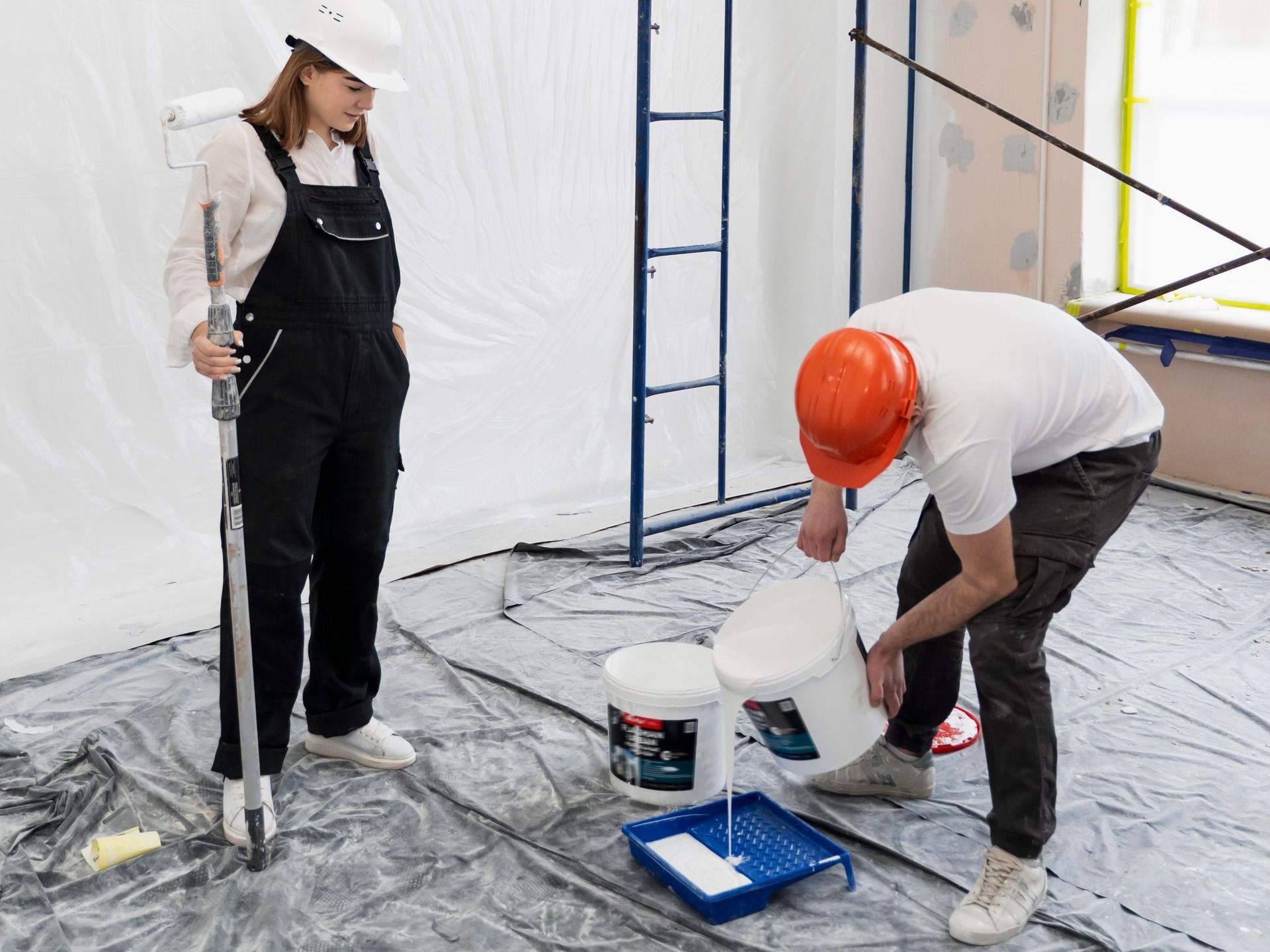 A man and a woman are painting a wall in a room.