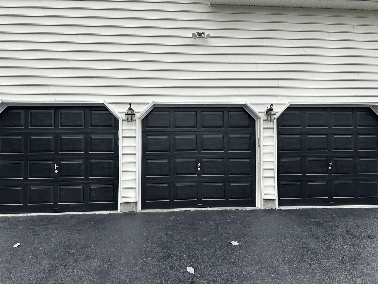 A black and white photo of three garage doors on a house.