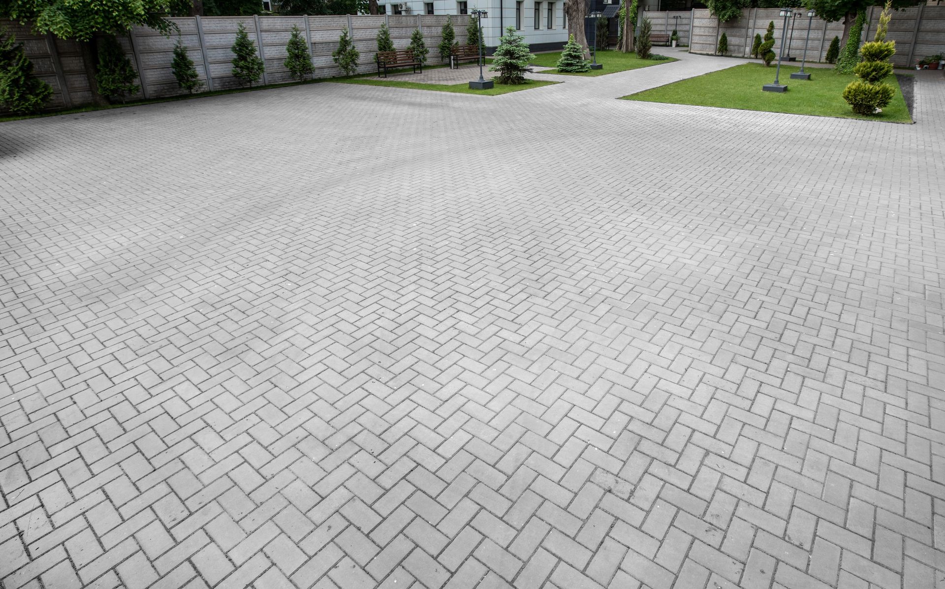 Brick paved parking area with some green landscaping and a concrete wall.