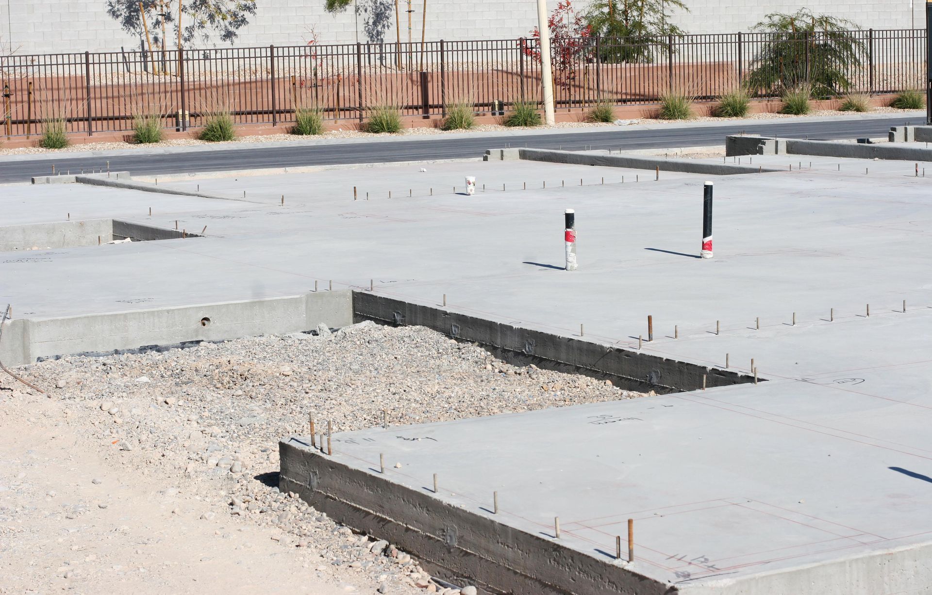 Foundation of a building under construction, concrete slab with exposed gravel, pipes, and rebar.