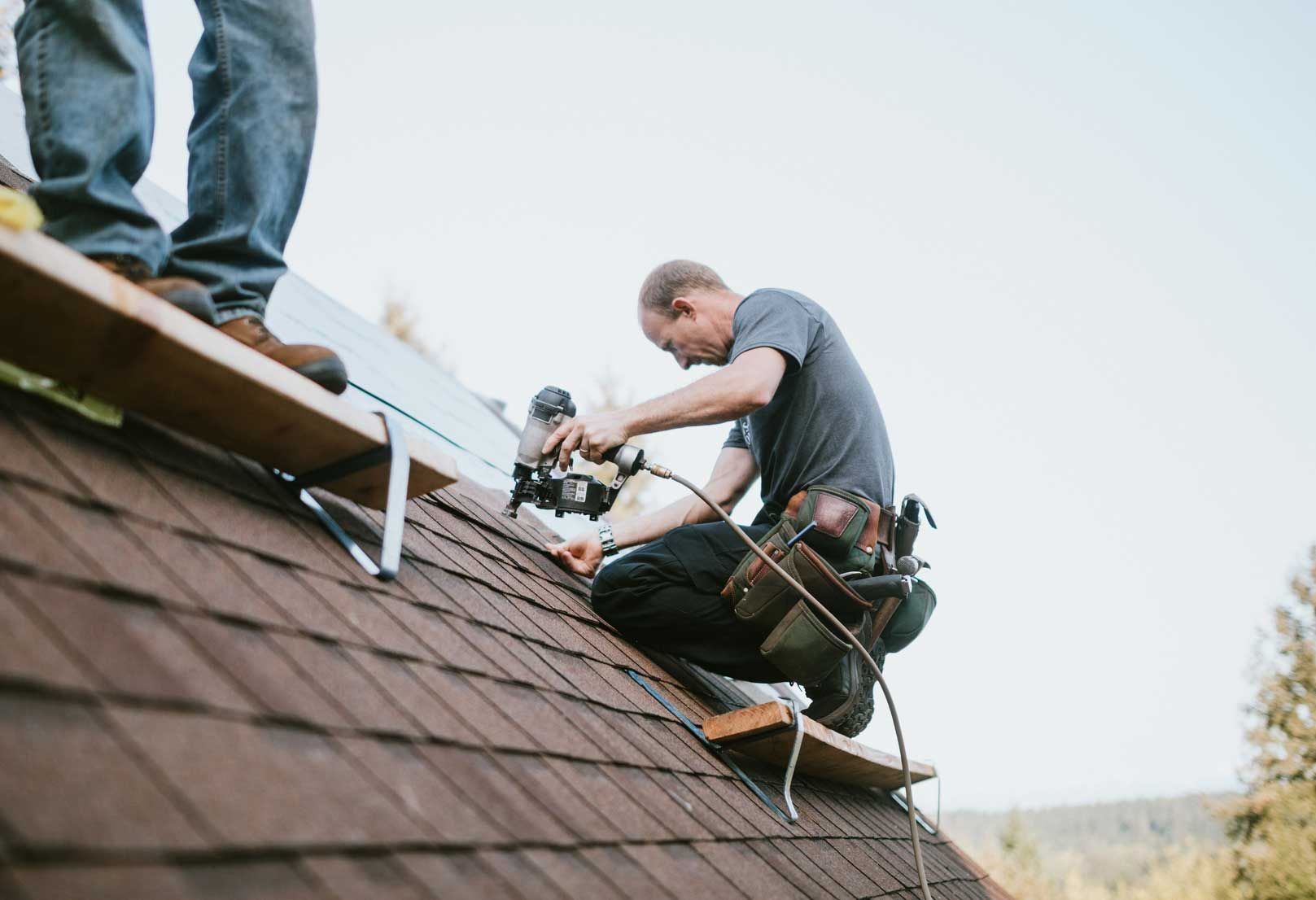 A man is kneeling on top of a roof working on a solar panel.