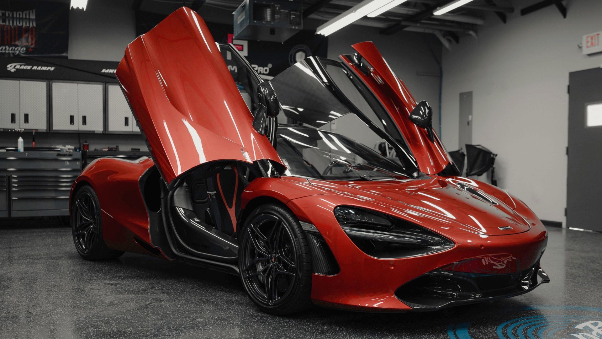 Red McLaren sports car with doors open in a garage.
