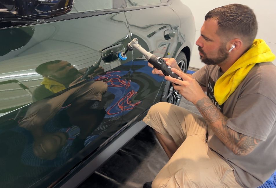 Man polishing a green car door with a power tool in a garage.