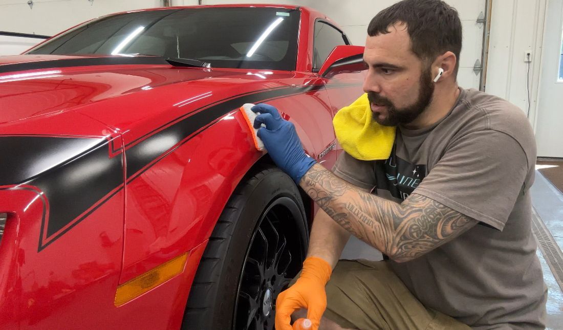 A man is cleaning the fender of a red sports car.