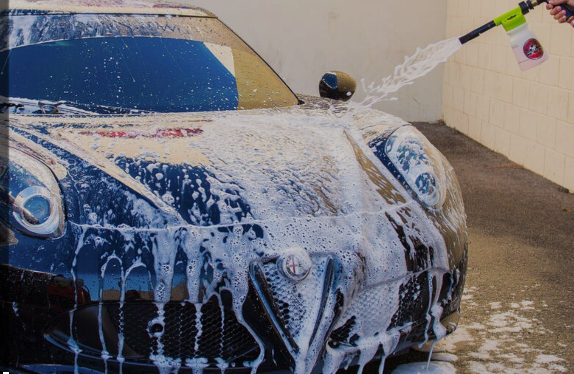 A person is spraying foam on a car with a hose