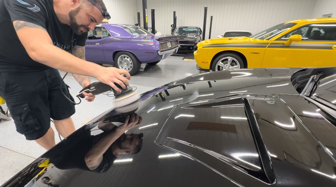 A man is polishing the hood of a car in a garage.