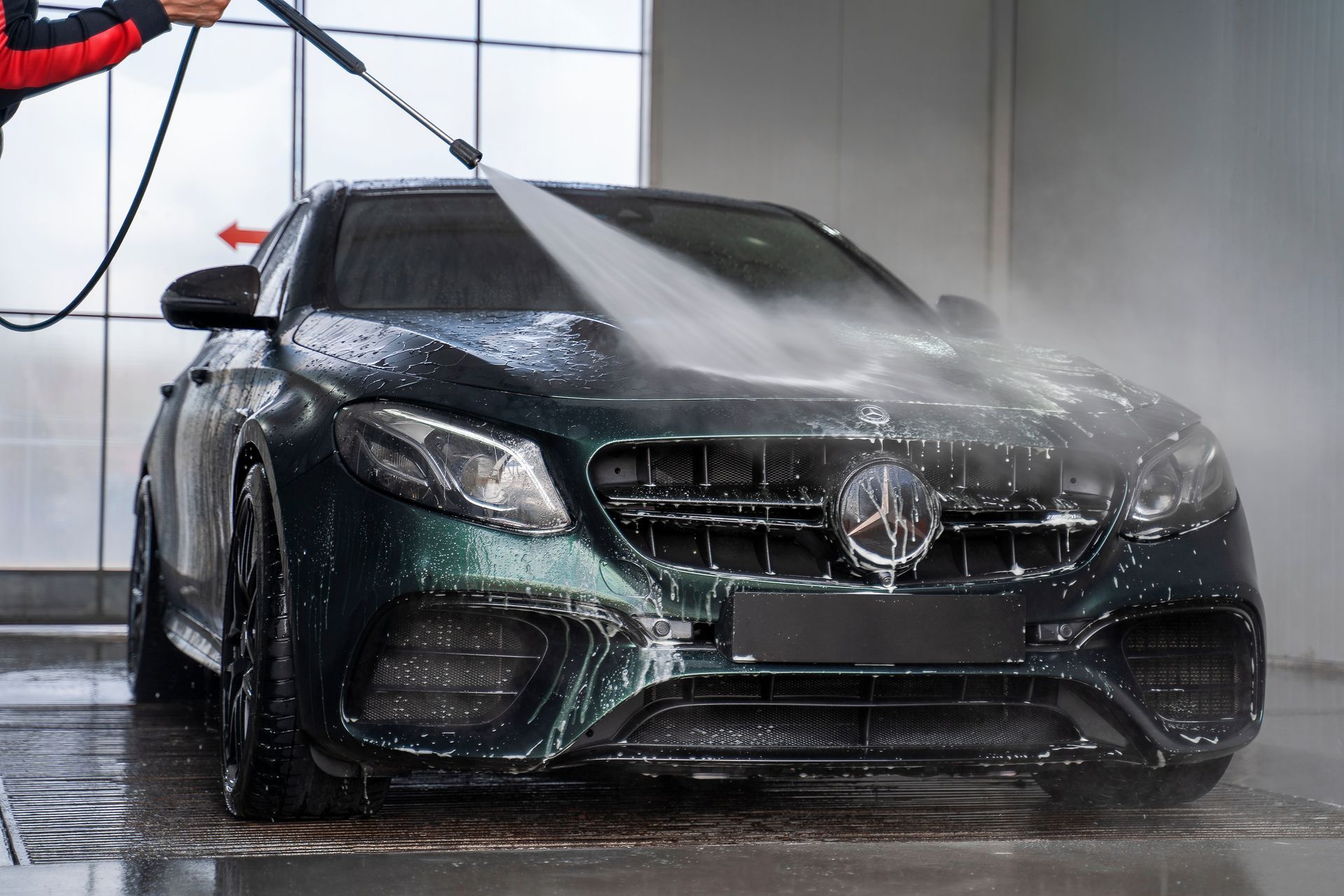 A dark green Mercedes-Benz being washed with a pressure washer, outdoors.