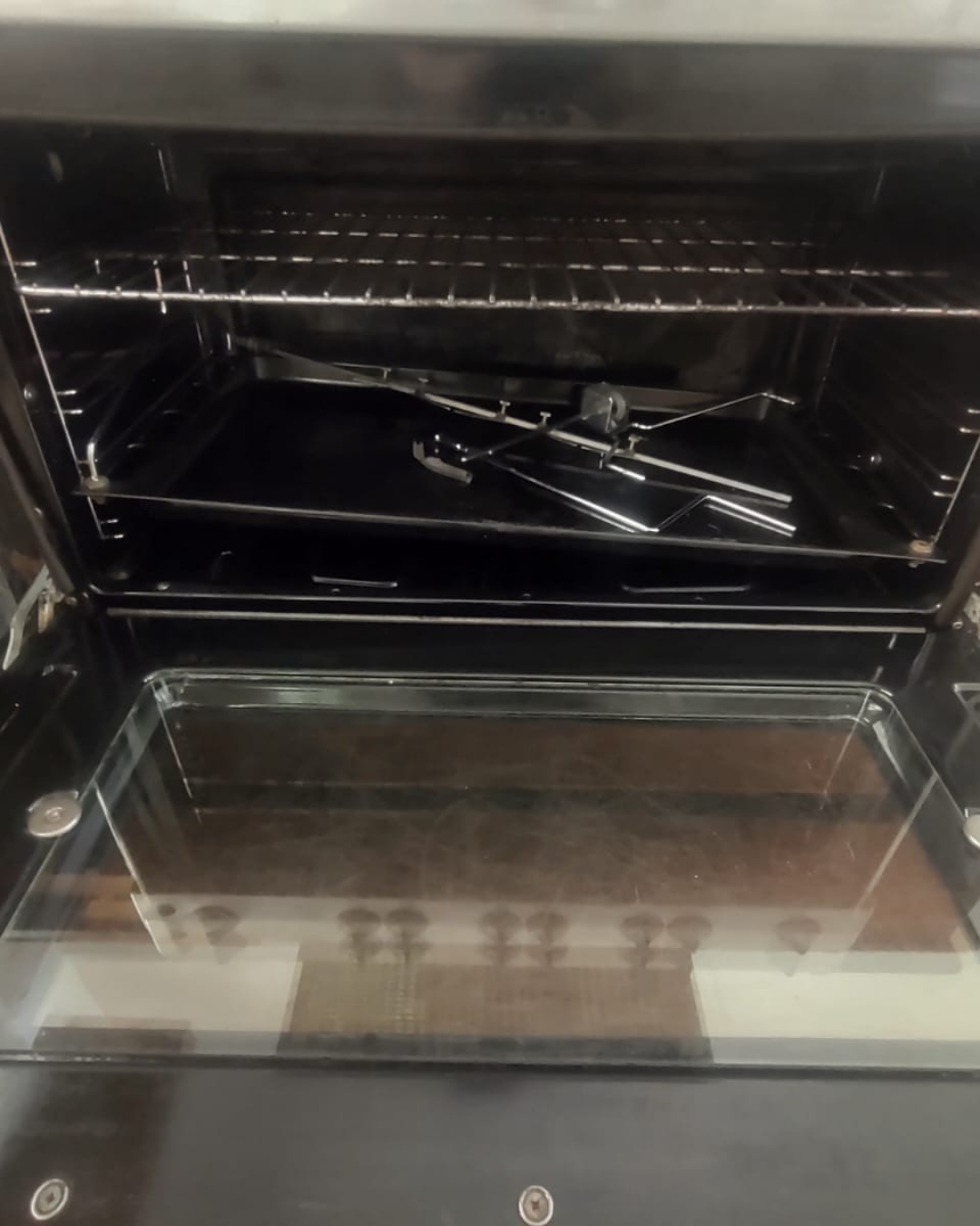 Interior de horno negro abierto con rejillas y bandeja. Puerta de cristal transparente.