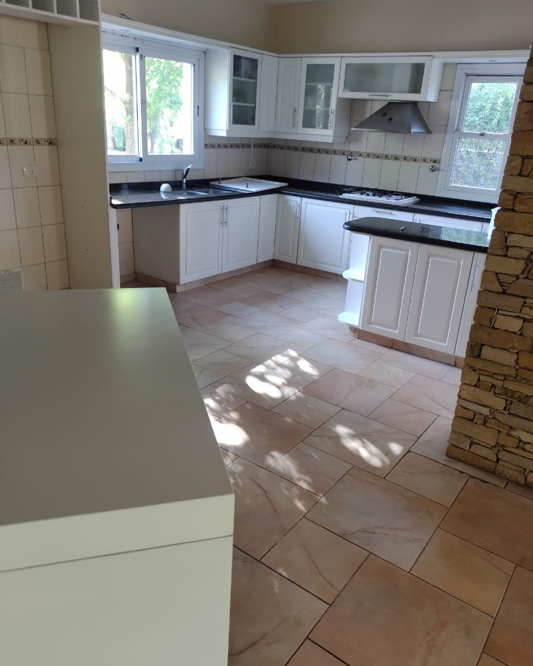 Cocina blanca con encimeras, gabinetes, electrodomésticos e isla de color negro; piso de baldosas.