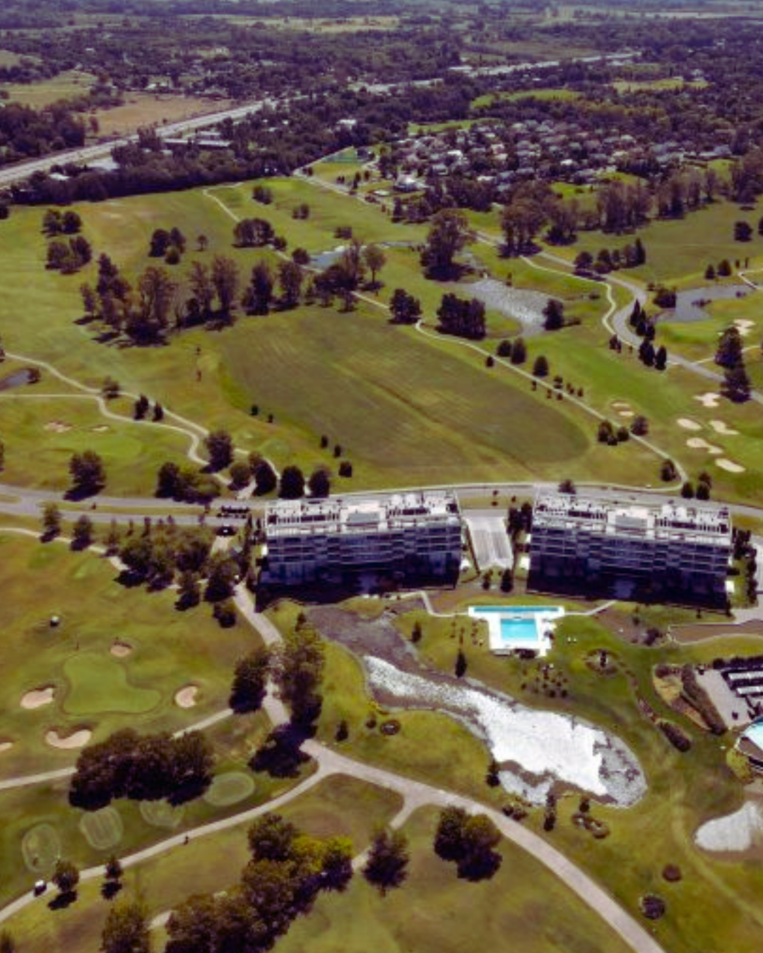 Vista aérea del campo de golf con calles verdes, dos edificios de apartamentos y una piscina.