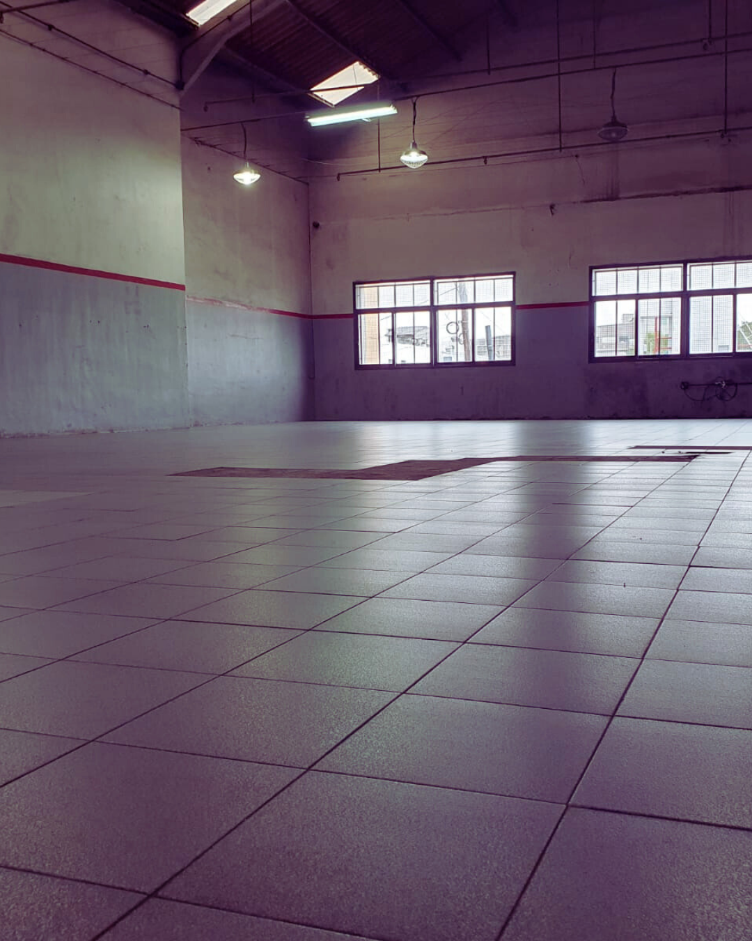 Gimnasio vacío con suelo de baldosas y ventanas.
