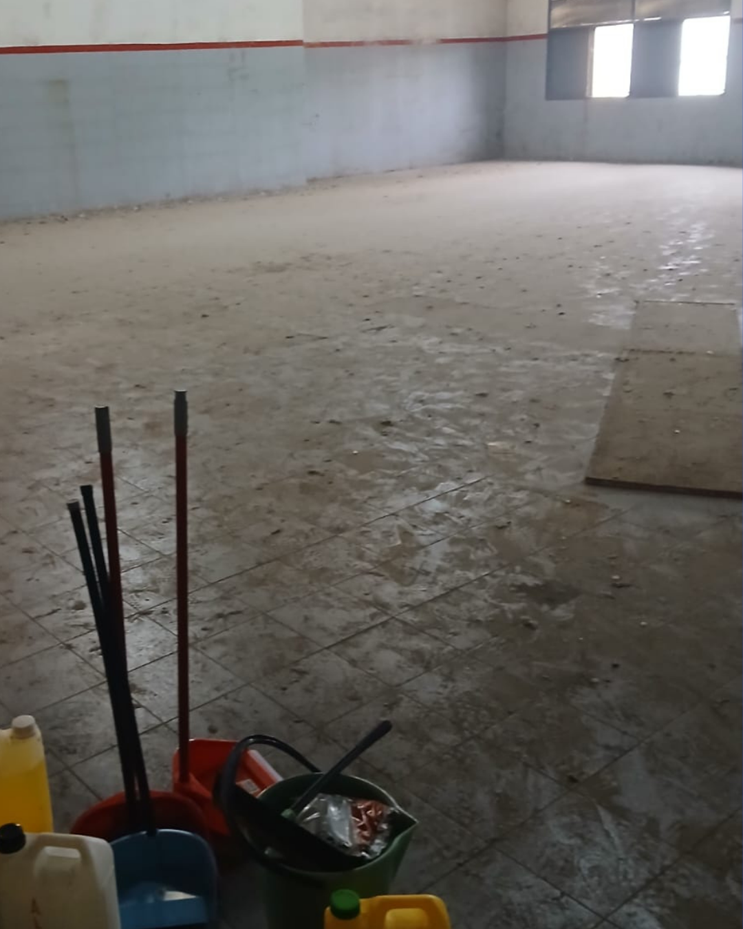 Habitación vacía con artículos de limpieza: escobas, cubos y jarras. El suelo está sucio.