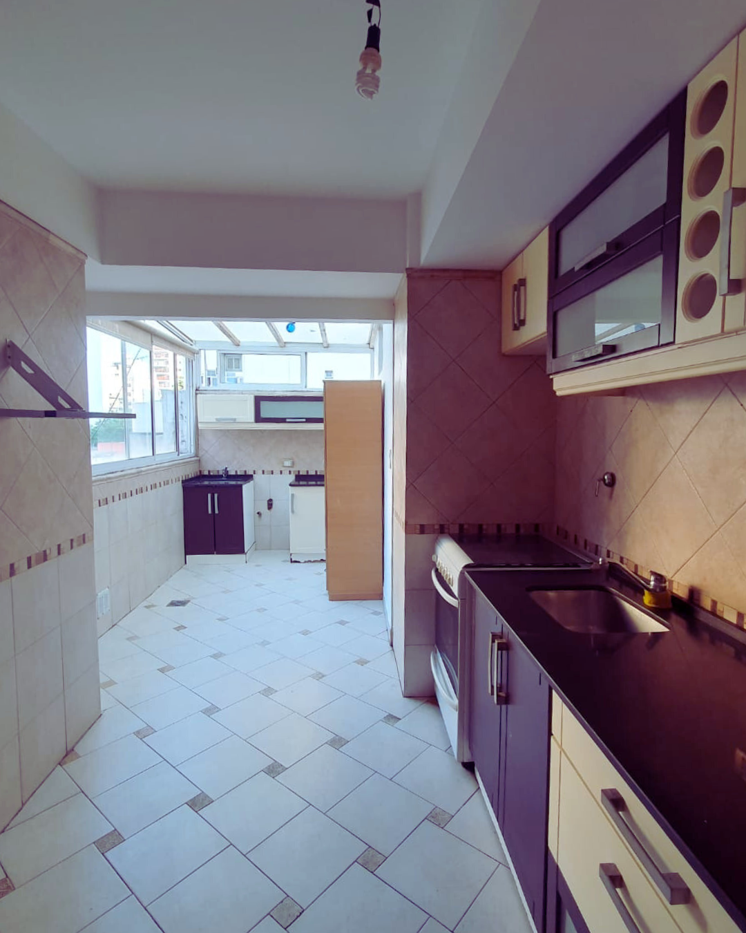 Cocina con piso de baldosas, gabinetes oscuros, estufa y área de ventanas a lo lejos.