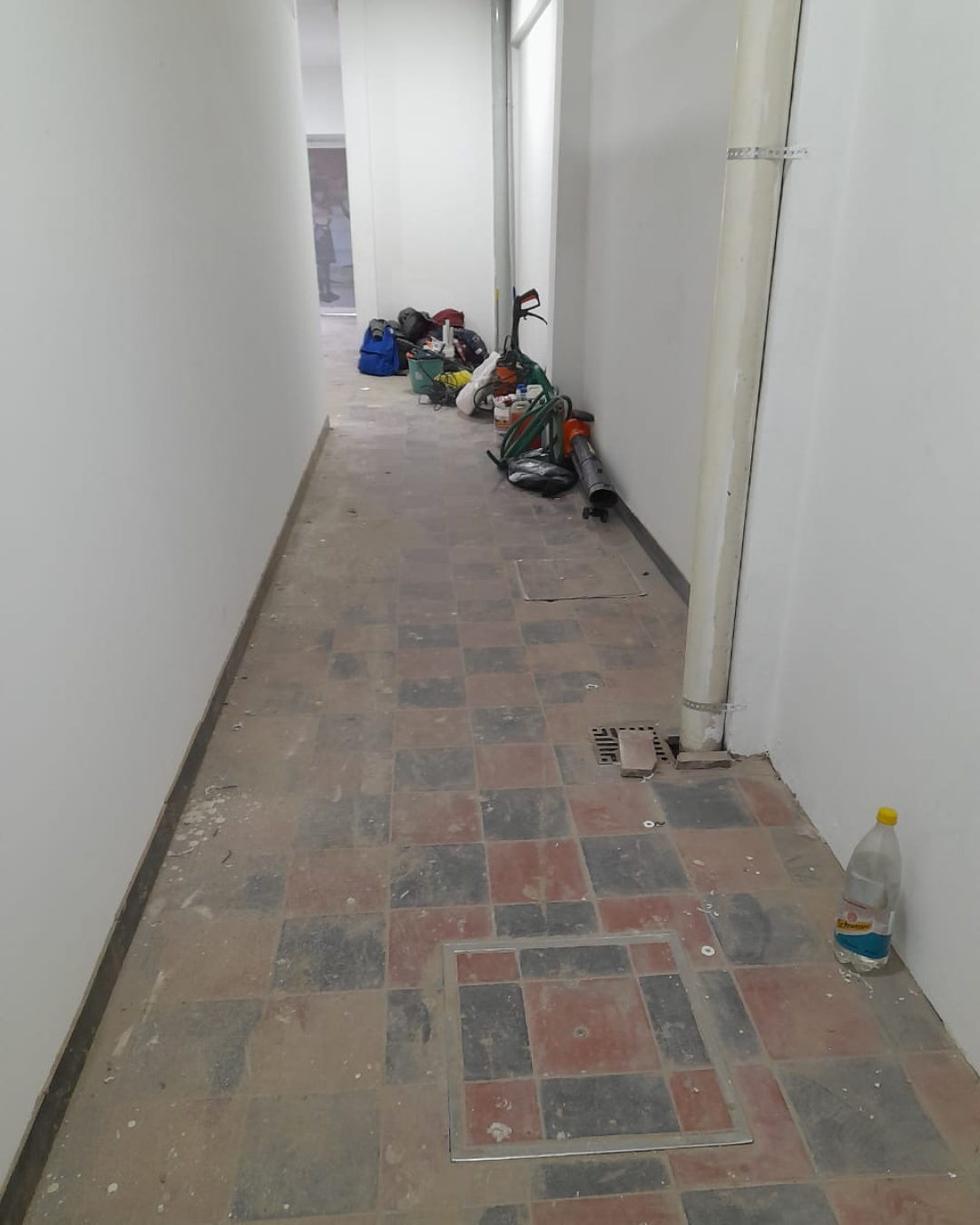 Pasillo estrecho con suelo de baldosas, paredes blancas y escombros.
