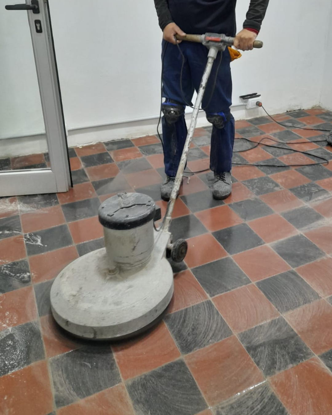 Persona que utiliza una máquina pulidora de suelos sobre un suelo de baldosas cuadriculadas.