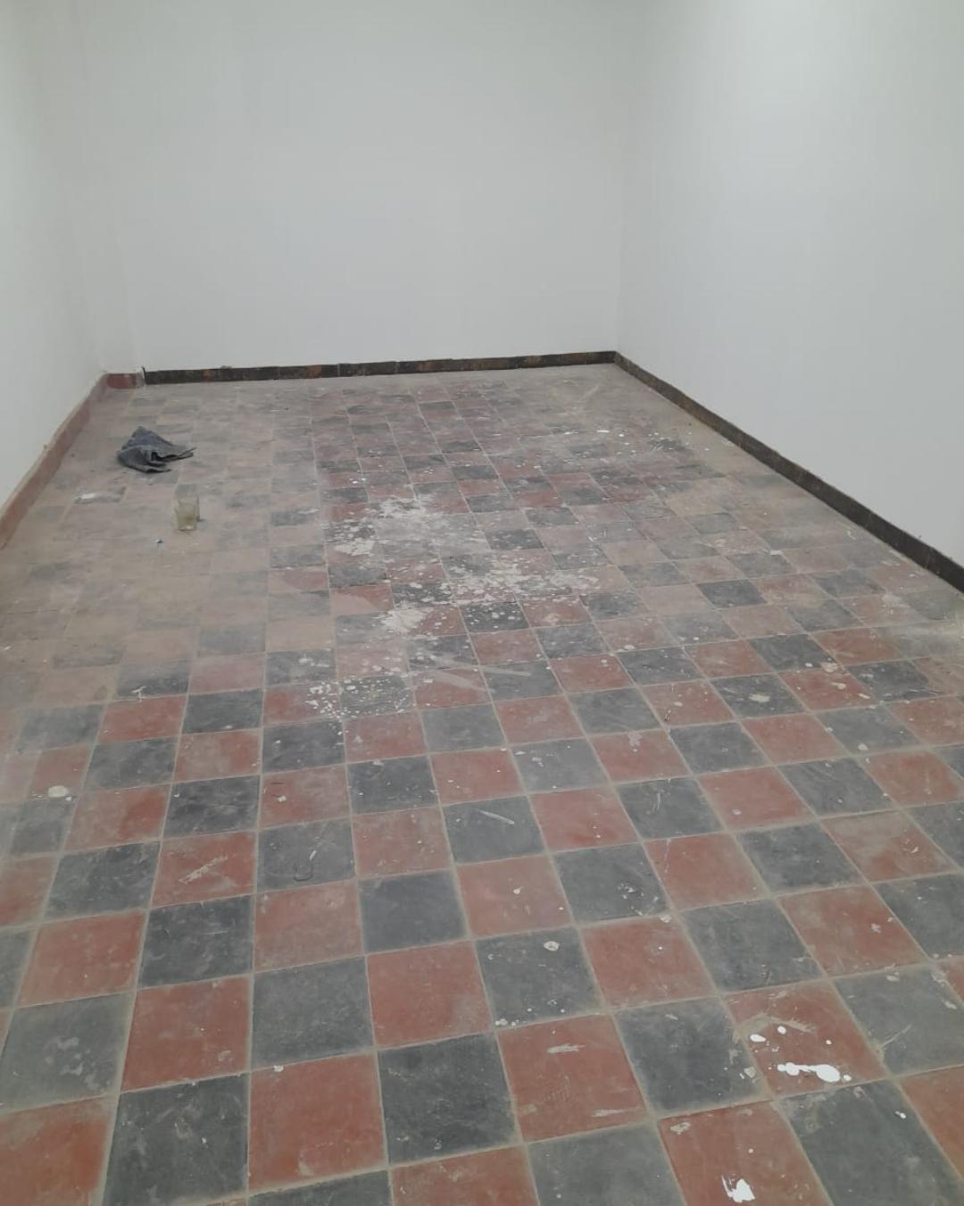 Habitación vacía con piso de baldosas a cuadros rojos y negros, paredes blancas y molduras negras.