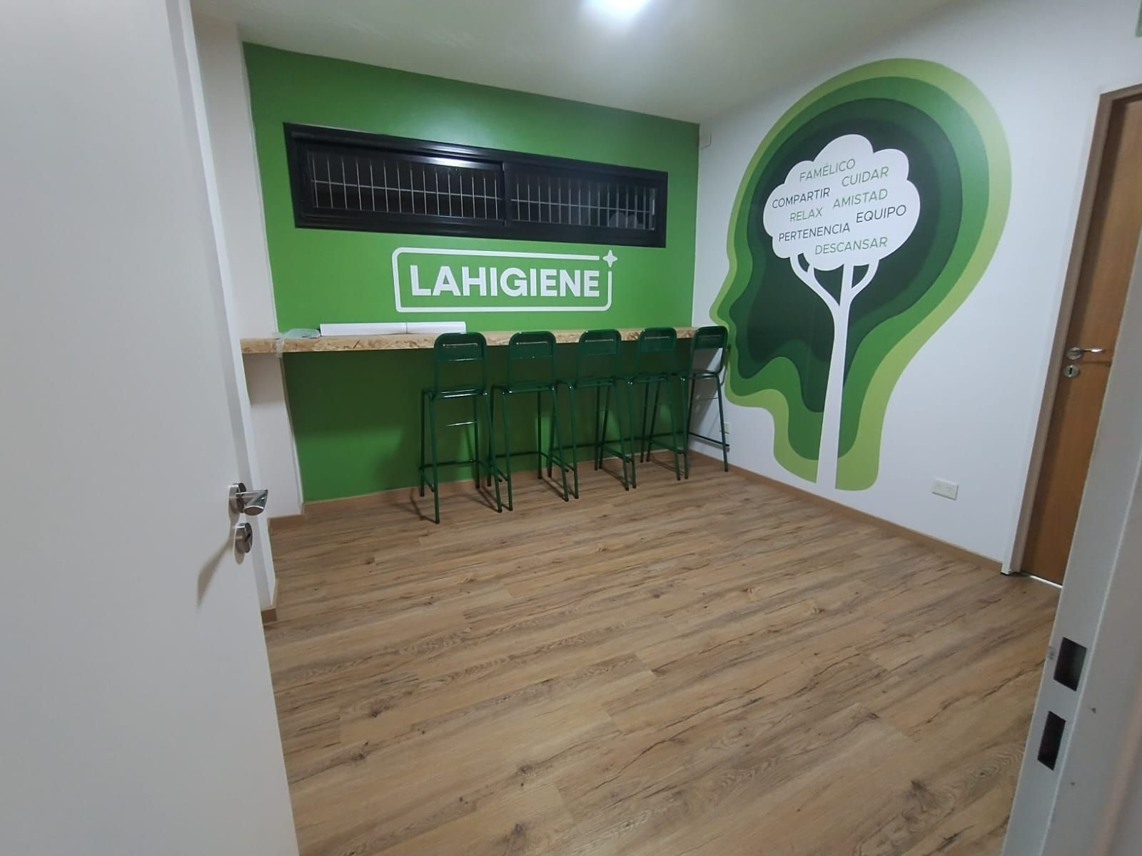 Habitación con paredes verdes y blancas, suelo de madera, taburetes de bar y un mural
