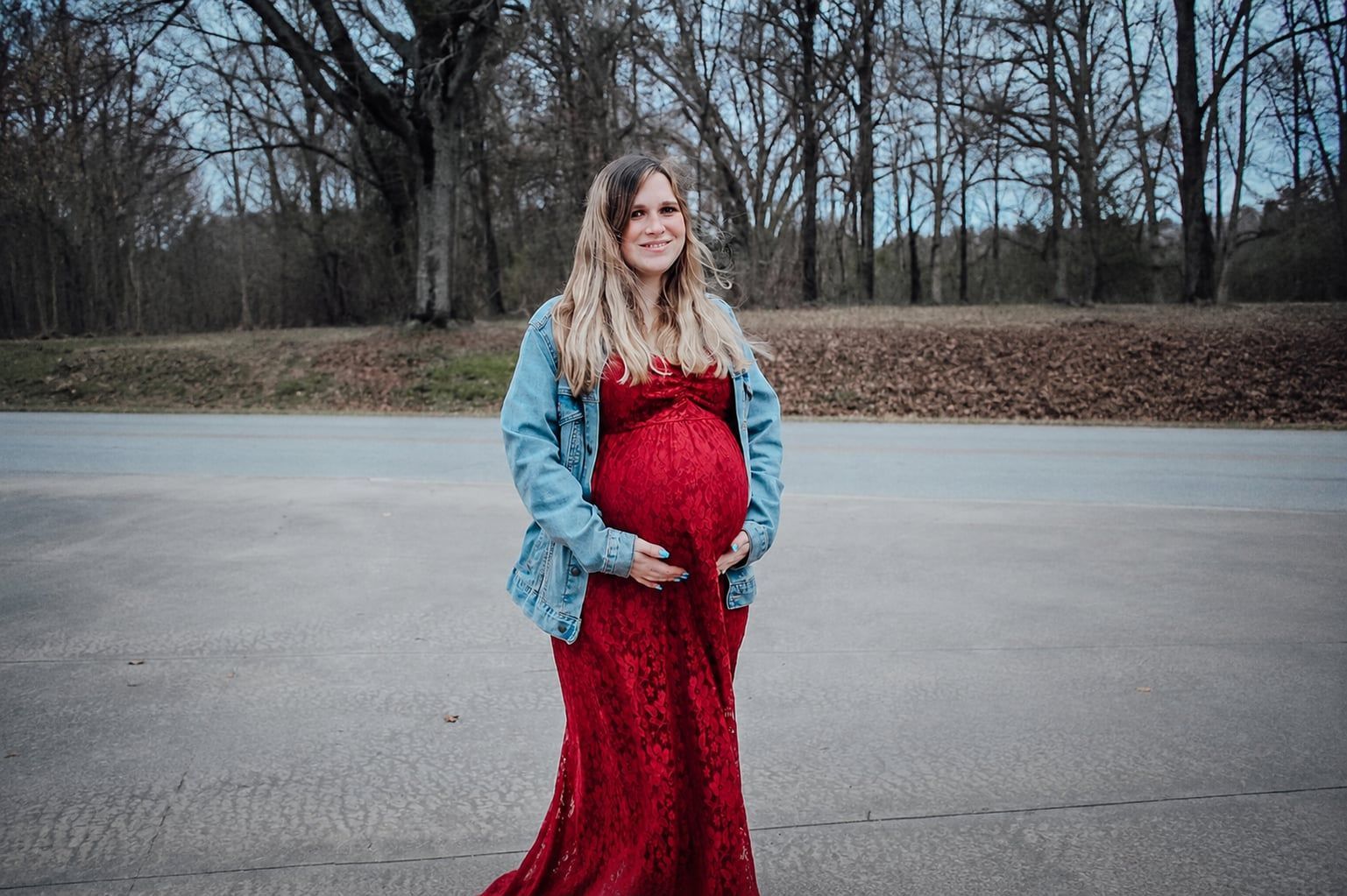 Pregnant woman in a red dress and blue shawl standing on a road outdoors