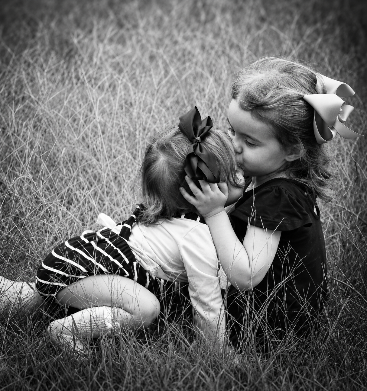 Black and white portrait of two young sisters sharing a sweet kiss outdoors – Shine Again Photography Newnan GA
