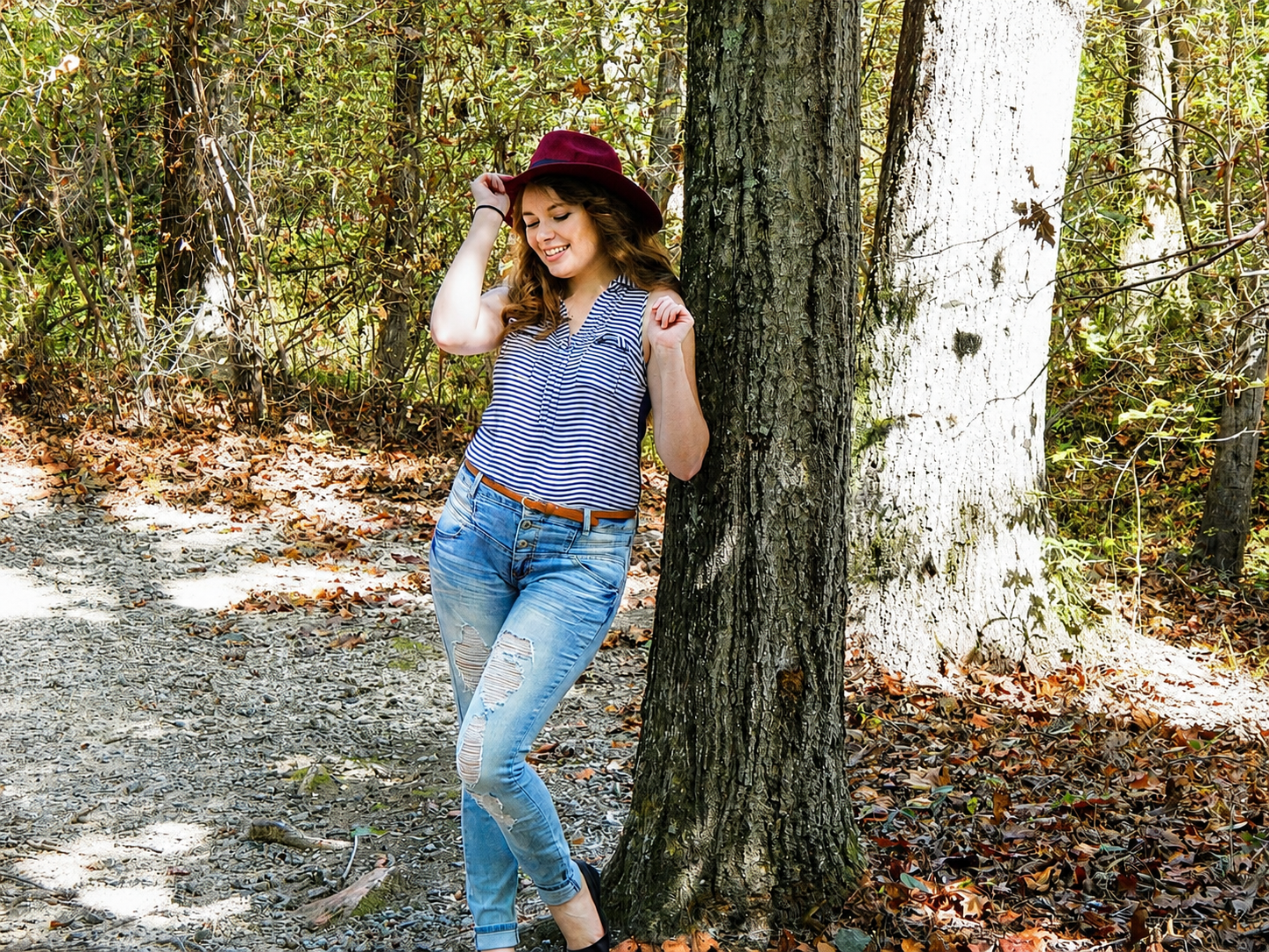 High school senior girl leaning against a tree in a forest wearing a burgundy hat – Shine Again Photography Newnan GA