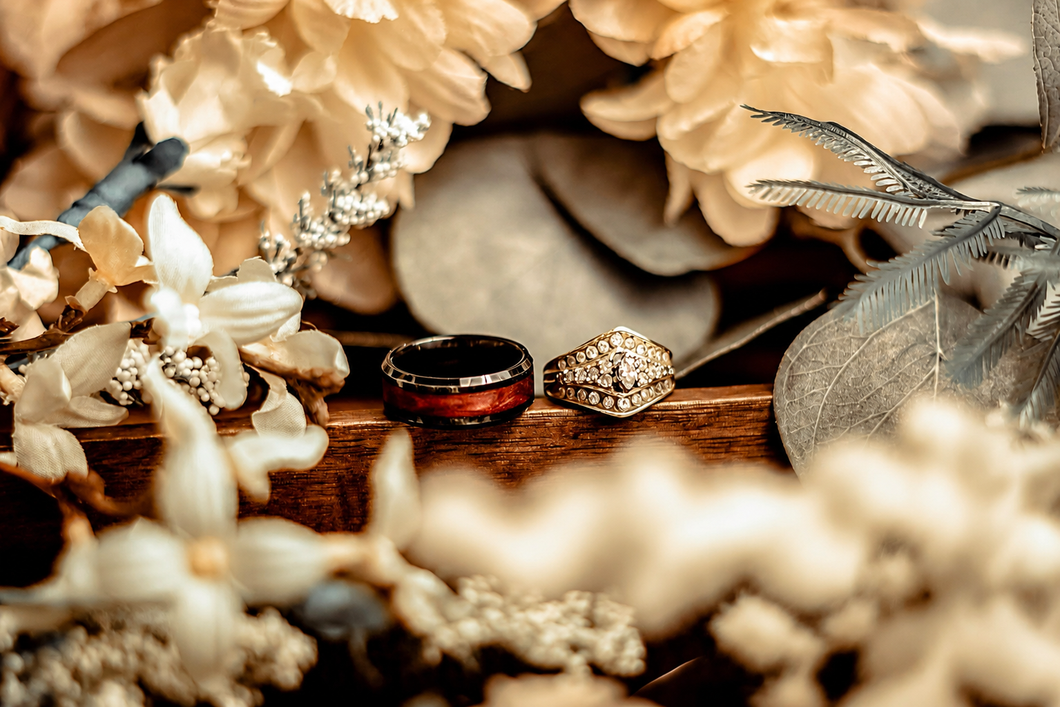 Close-up of diamond wedding ring and bands displayed on wood with white floral bouquet – Shine Again Photography Newnan GA