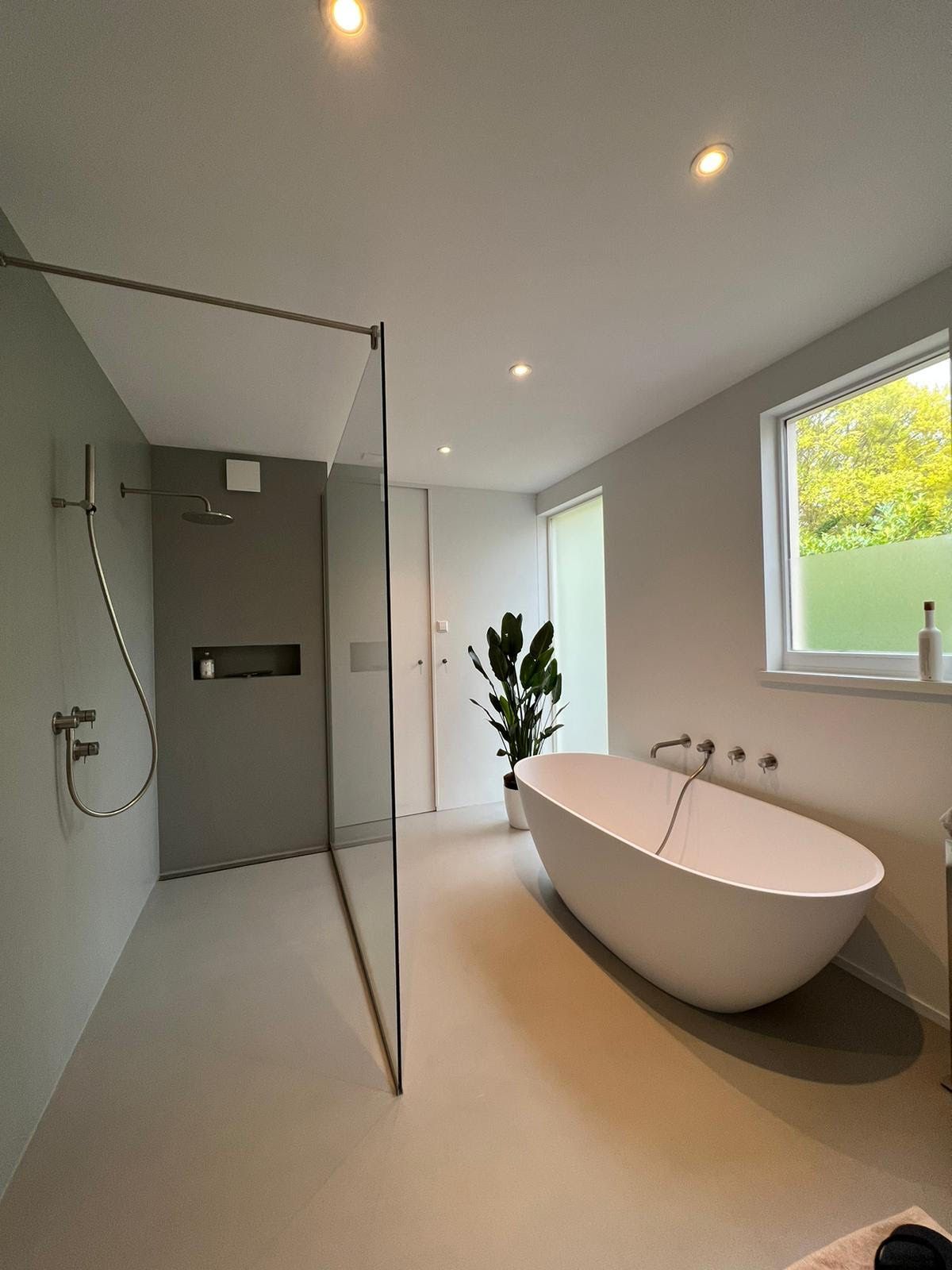 Moderne badkamer met glazen douchecabine, vrijstaand bad en groot raam met uitzicht op het groen.