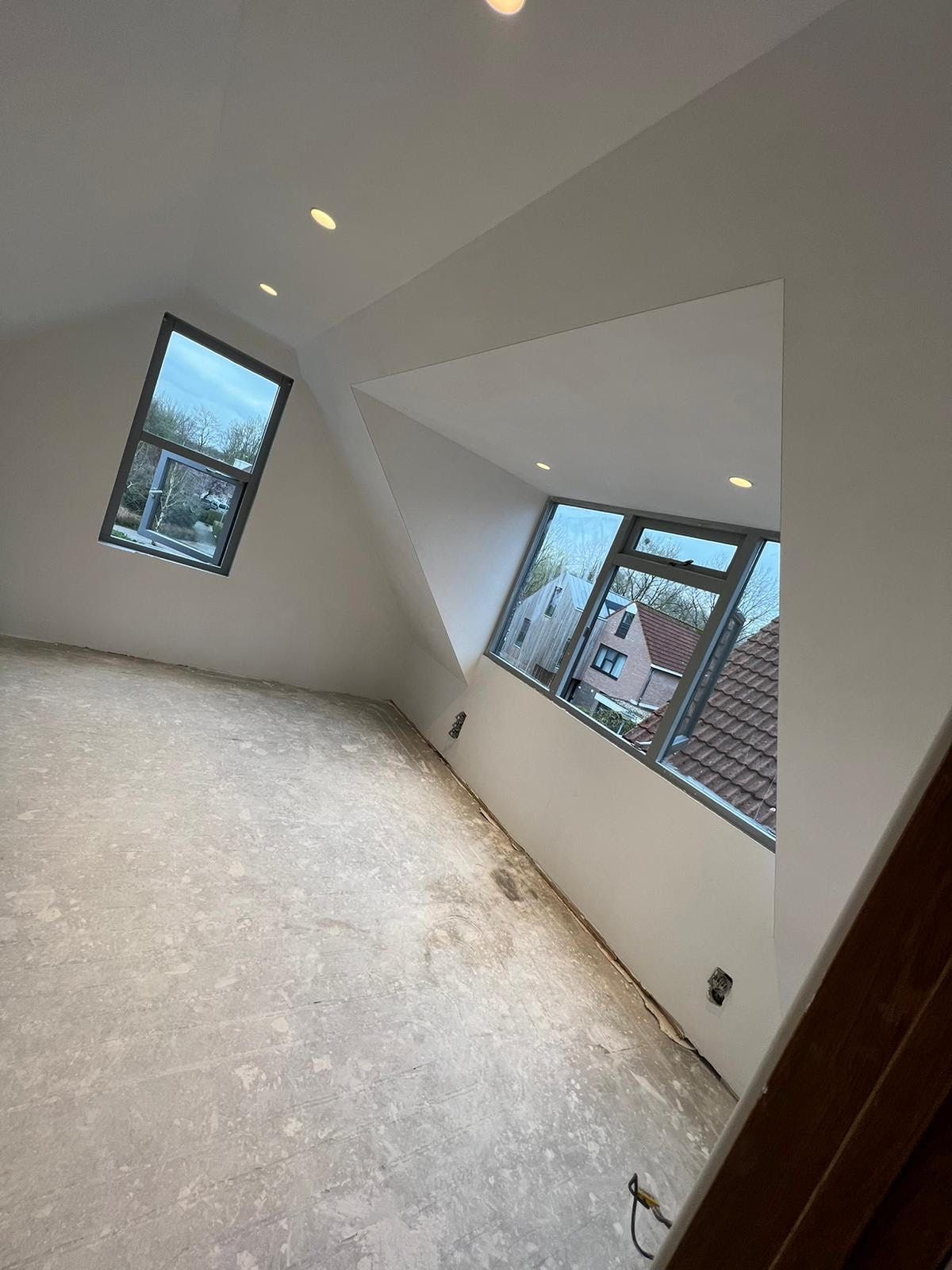 Lege witte kamer met schuine muren, ramen en onafgewerkte vloerbedekking.