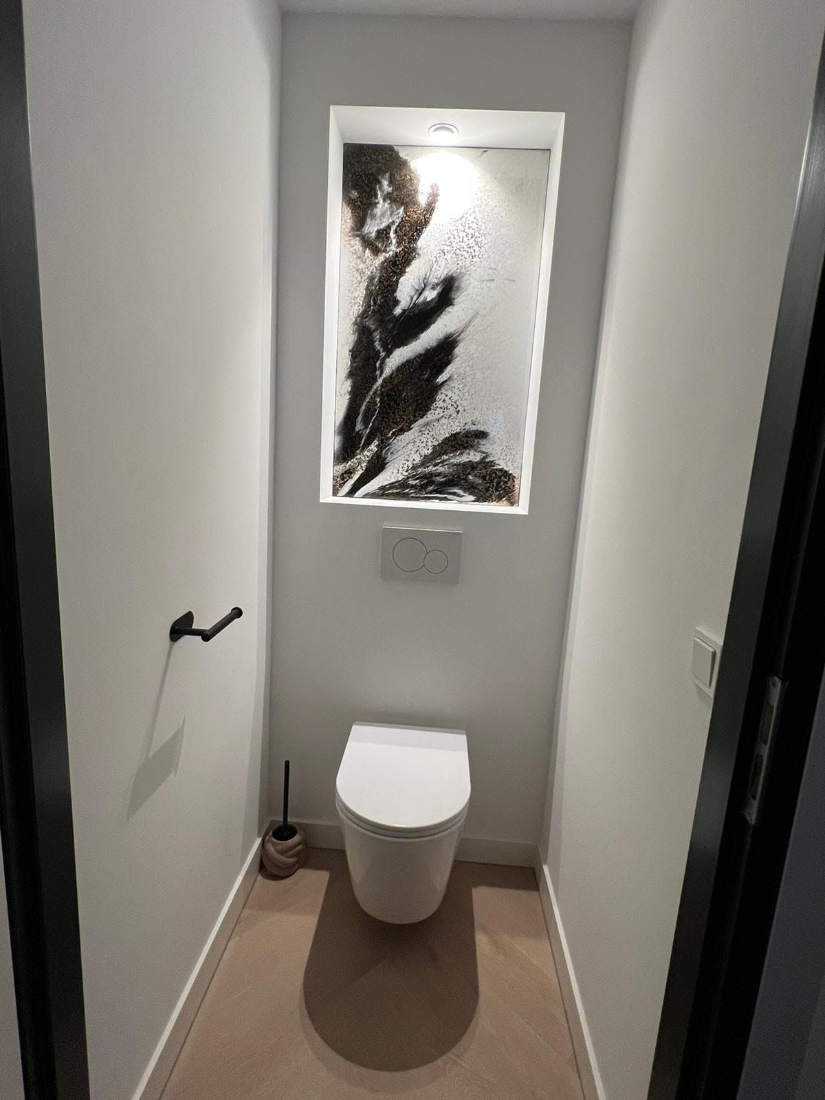 Kleine, moderne toiletruimte met een aan de muur gemonteerd toilet en abstracte kunst erboven.