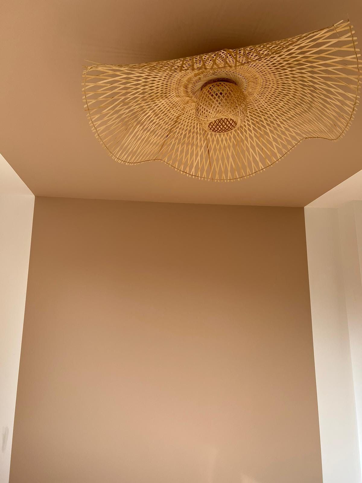 Beige kamerhoek met een plafondlamp van geweven rotan in het midden van het plafond.