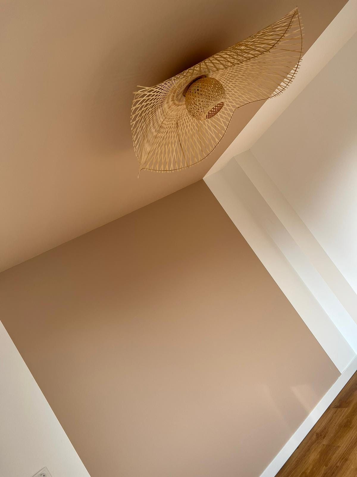 Een lege beige hoek in een kamer met een geweven hanglamp aan het plafond.
