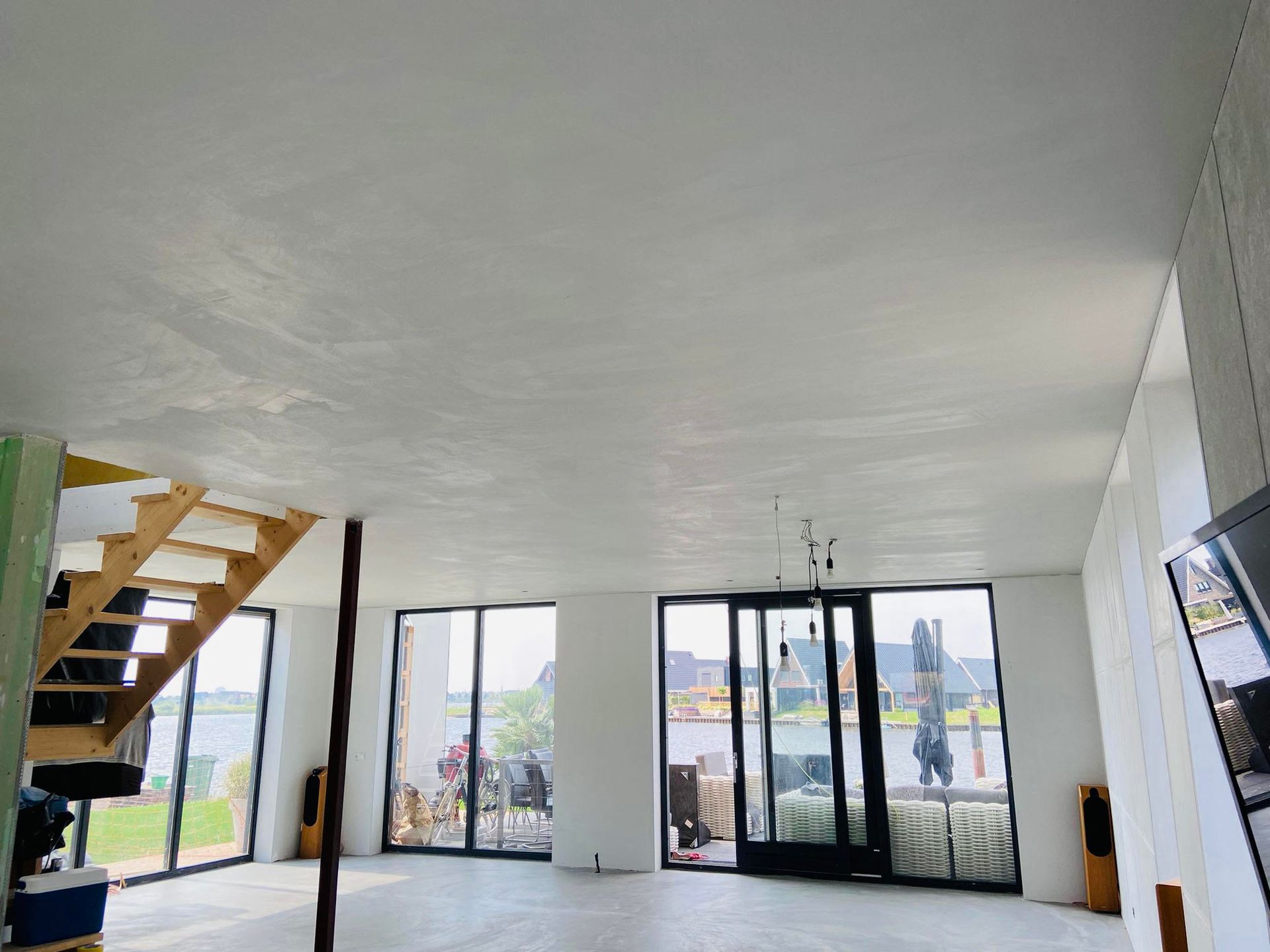Lege, moderne woonkamer met witte muren, glazen deuren, een trap en grote ramen met uitzicht naar buiten.