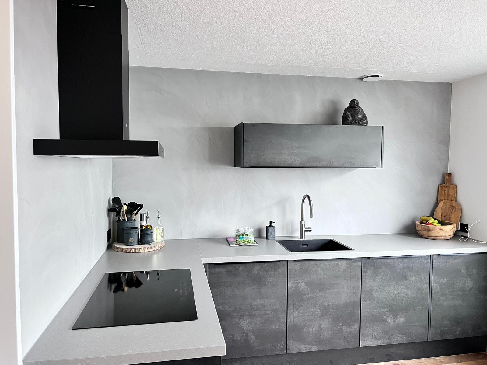 Moderne grijze keuken met zwarte kookplaat, afzuigkap, zwevende planken en spoelbak aan de rechterkant.