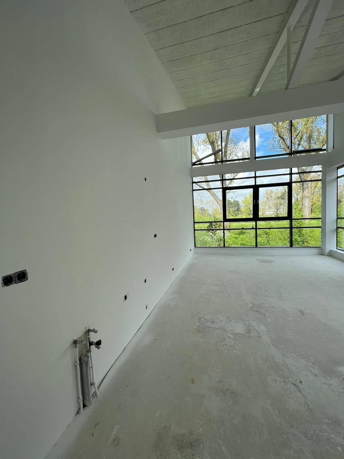 Lege witte ruimte met grote ramen en een schuin plafond, in aanbouw.