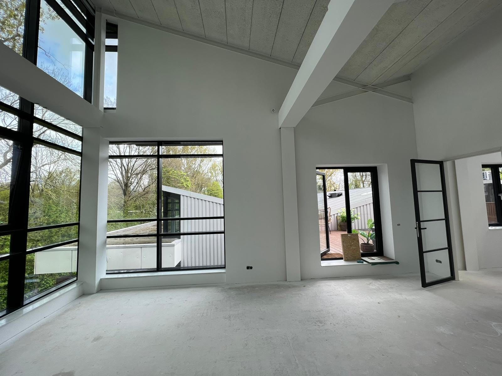 Lichte, lege, moderne kamer met hoge plafonds, witte muren en grote ramen van vloer tot plafond.