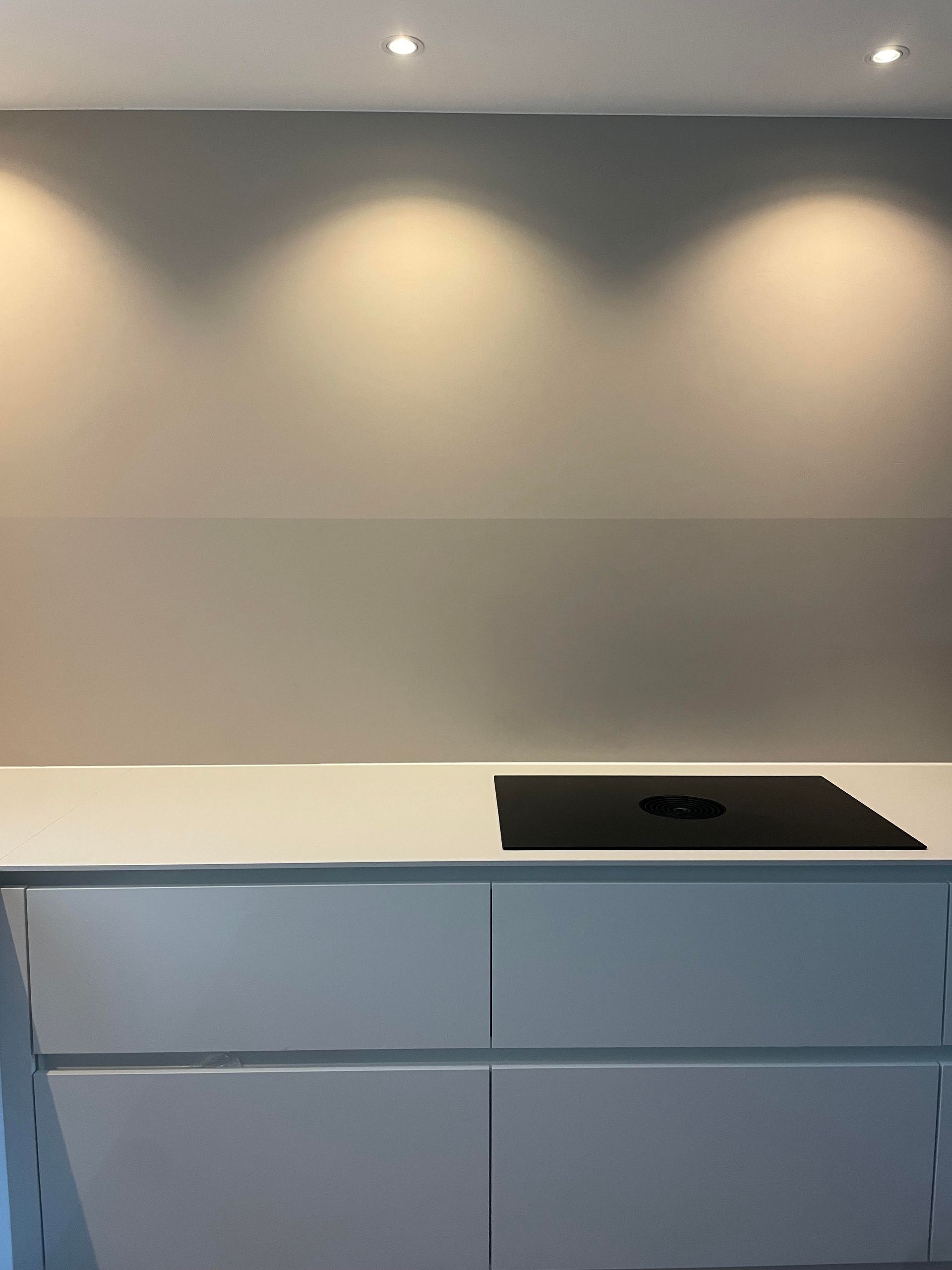 Moderne keuken met wit aanrechtblad, zwarte kookplaat en lichtgrijze kasten onder inbouwverlichting.