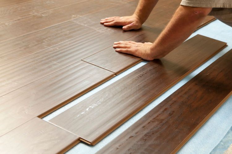 Un rodillo de pintura aplica un acabado brillante a un piso de madera, mostrando un contraste