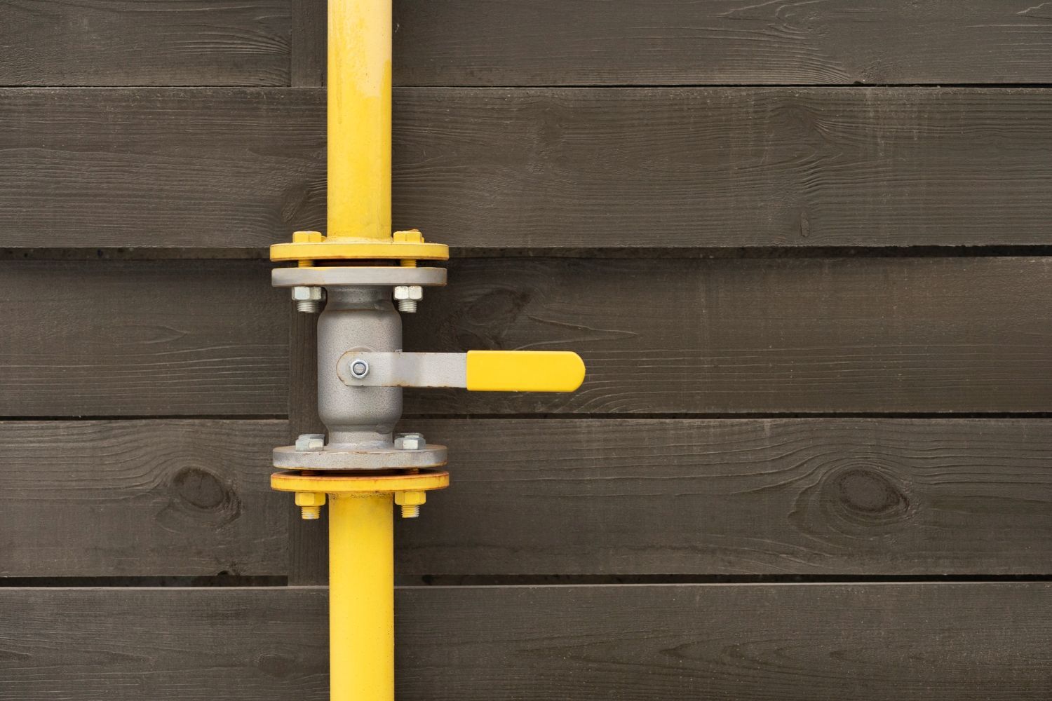 Yellow gas pipe with shutoff valve against dark wood siding