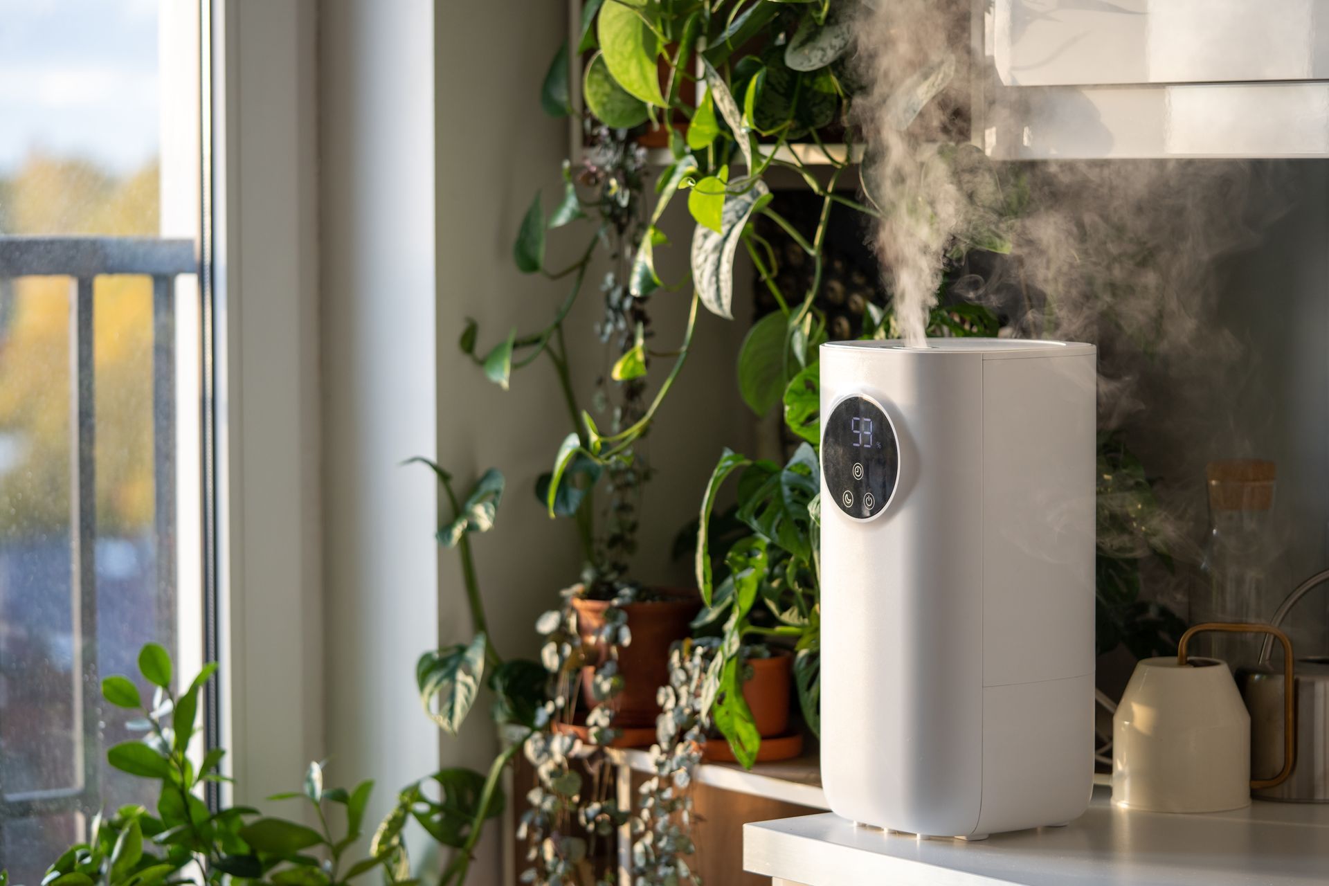 White air purifier on a windowsill beside houseplants, with steam rising in a sunlit room.