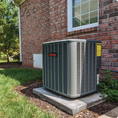 An air conditioner is sitting on the side of a brick house.