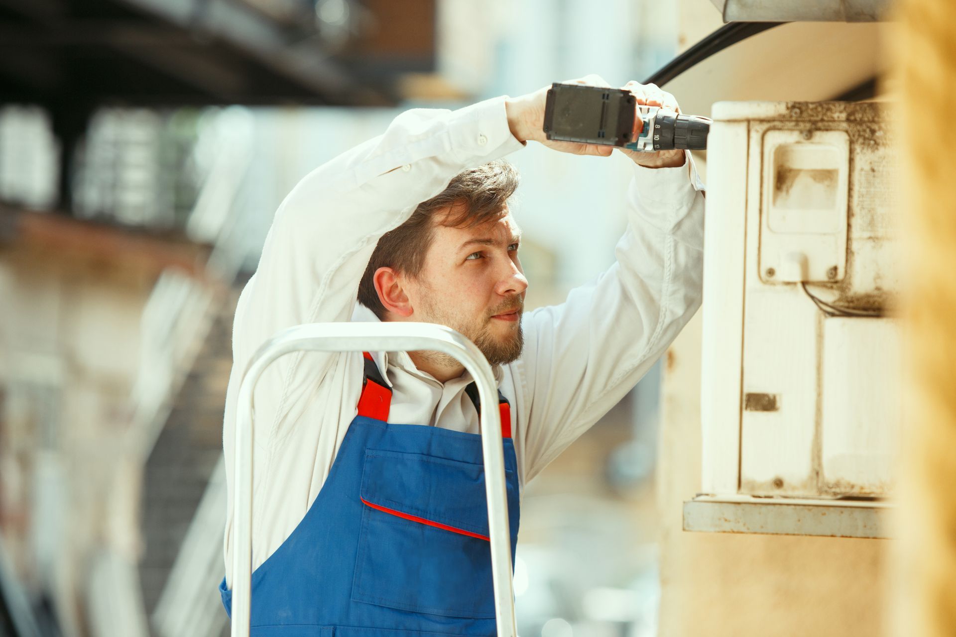 A man is using a drill to fix an air conditioner on a building.