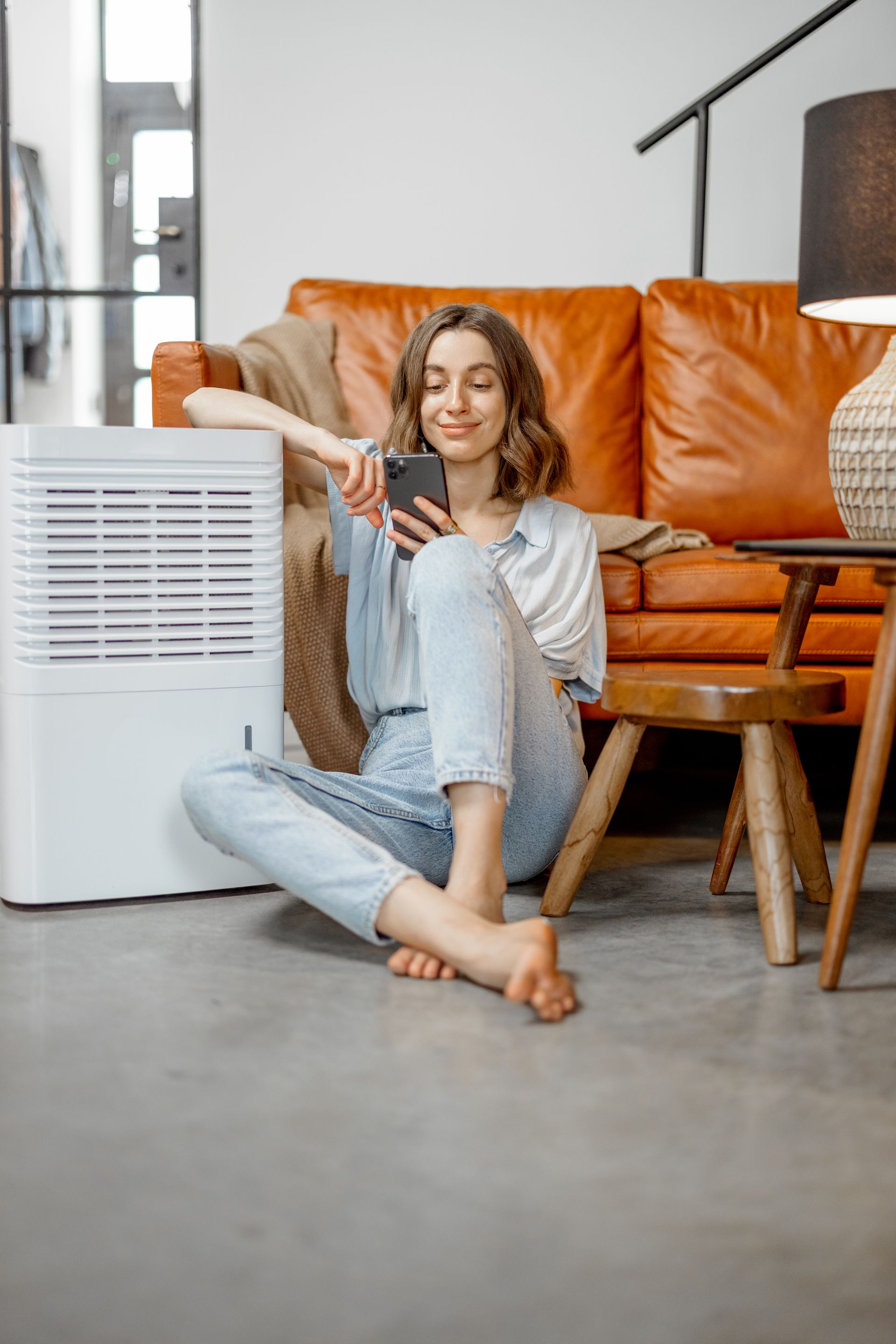 A woman is sitting on the floor in front of a couch using a cell phone.