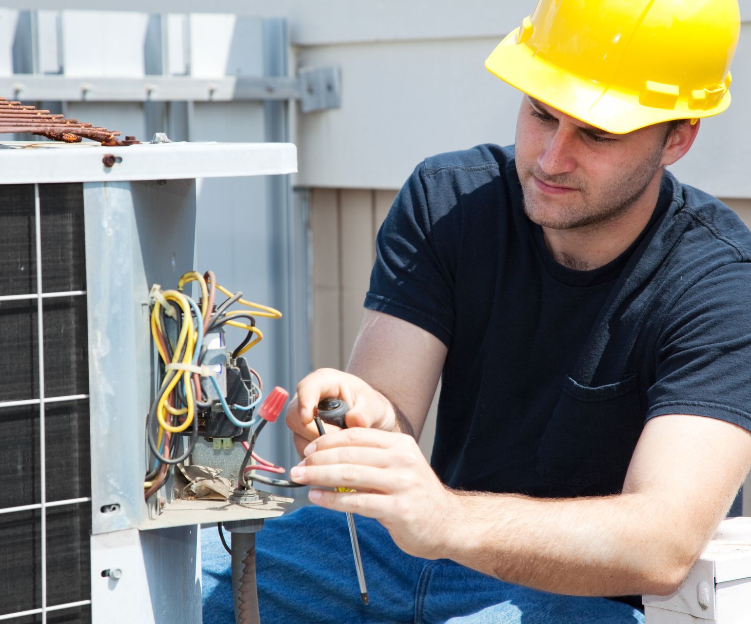 A man wearing a hard hat is working on an air conditioner