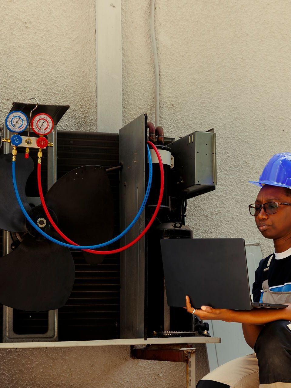 A man wearing a blue hard hat is working on an air conditioner