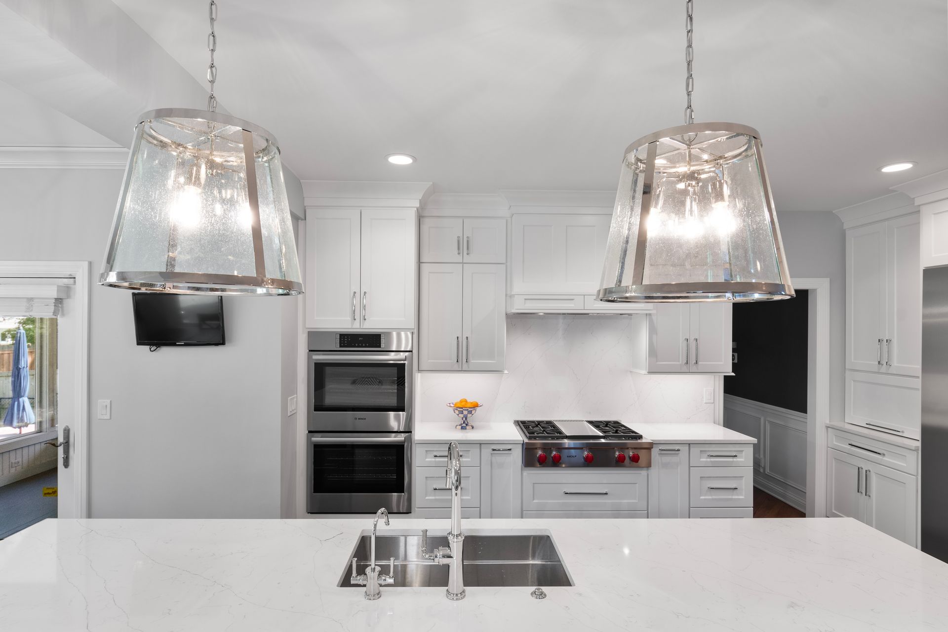 A kitchen with white cabinets , stainless steel appliances , a sink , and two pendant lights.