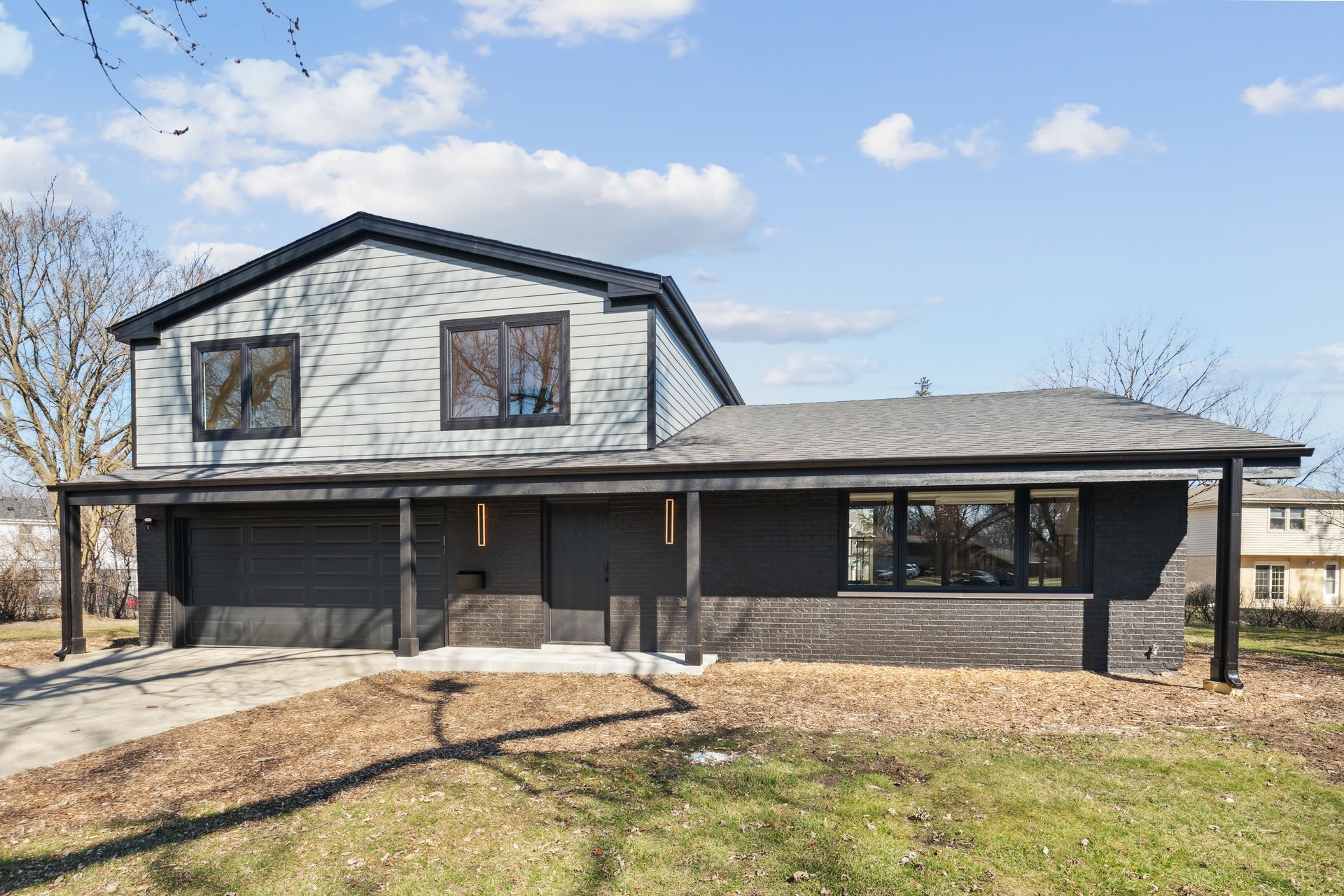 A large house with a black garage door is sitting on top of a lush green field.
