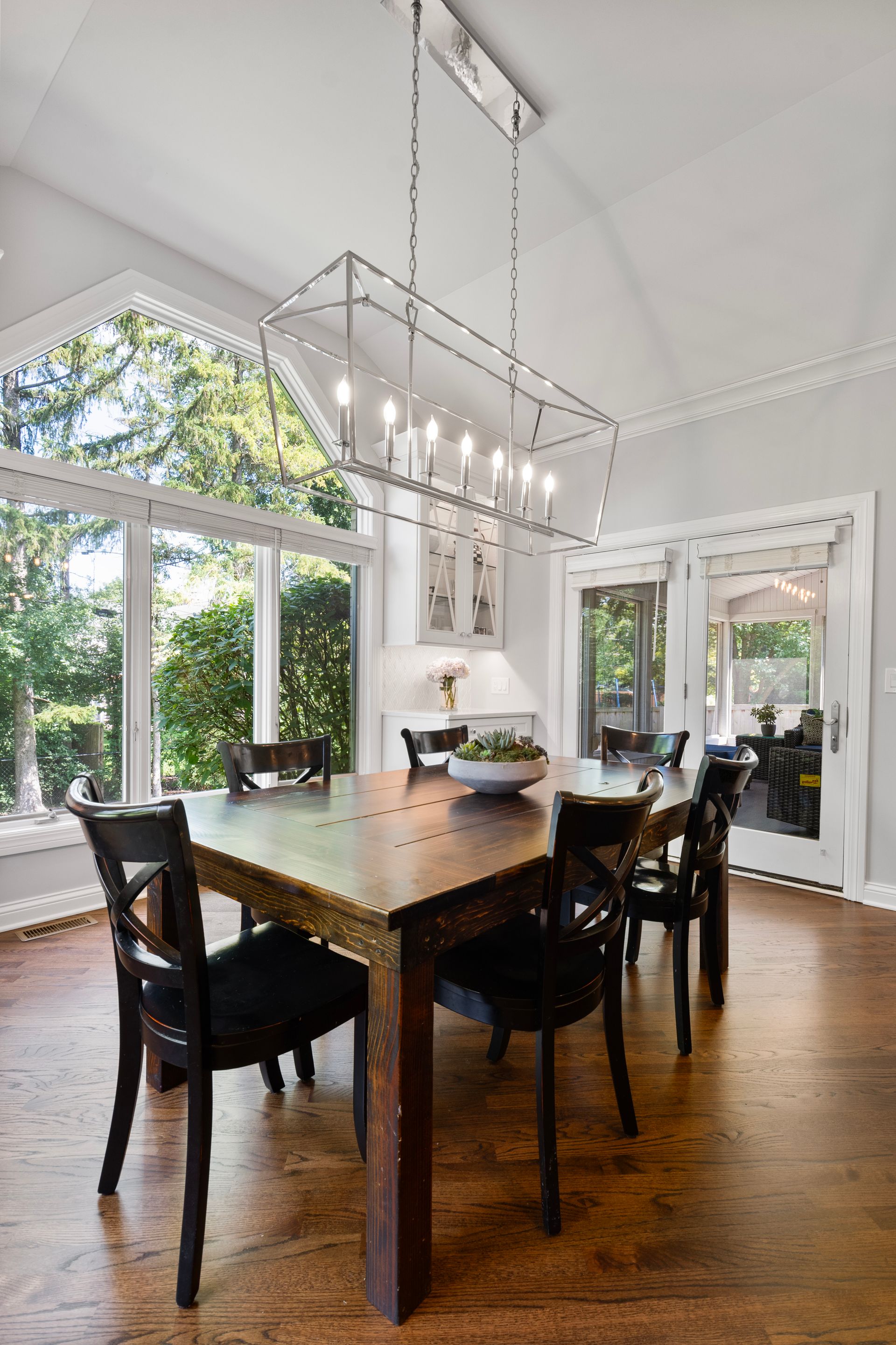 A dining room with a wooden table and chairs and a large window.