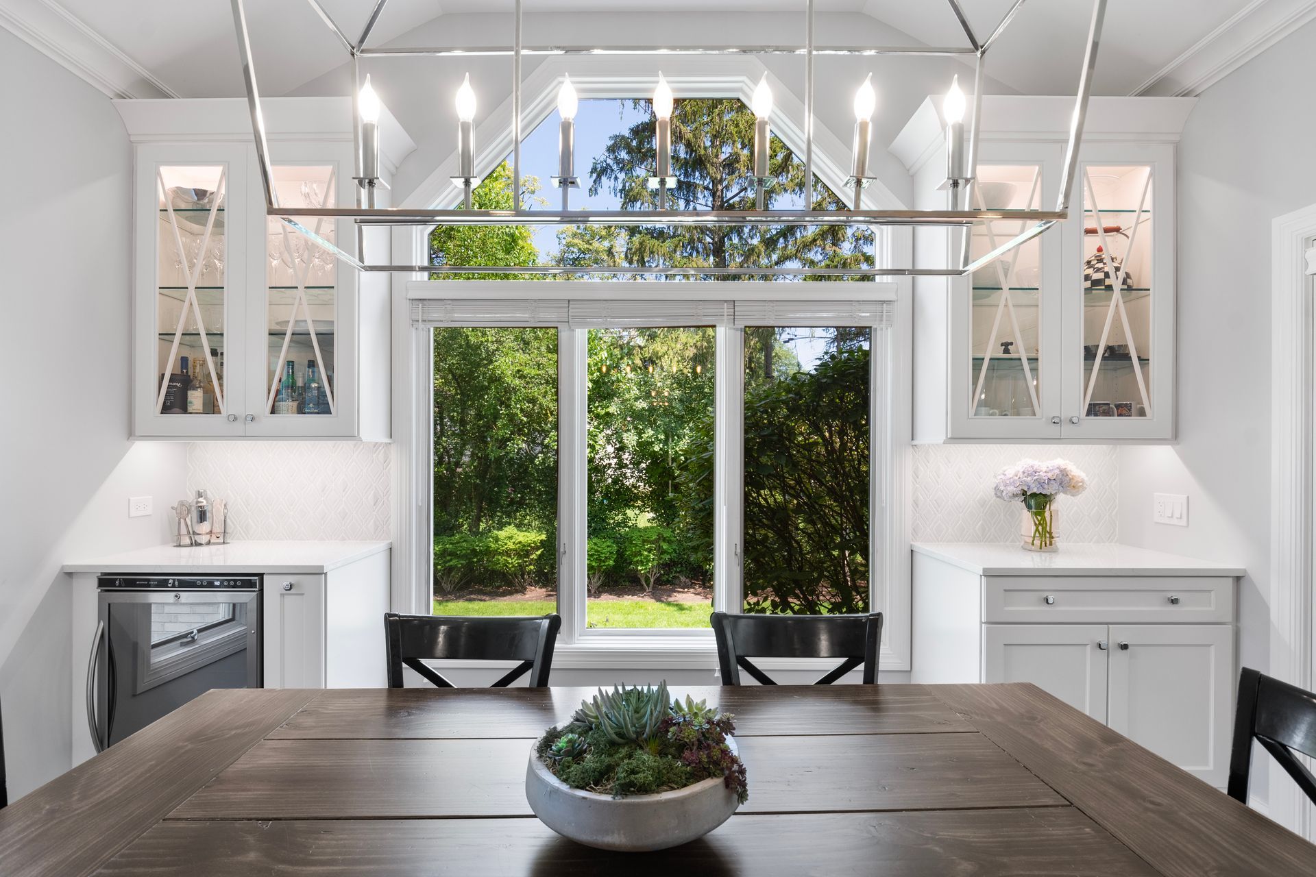 A dining room with a wooden table and chairs and a large window.