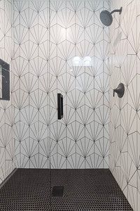 A shower with black and white tiles and a black floor.
